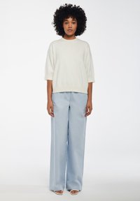 Maglione leggero oversize con maniche corte abbinato a pantaloni larghi di un tenue blu chiaro con sottili motivi a pois e sandali aperti.