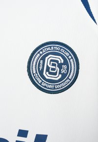 Λευκό αθλητικό ύφασμα με κυκλικό μπλε κεντητό λογότυπο που αναγράφει "ATHLETIC CLUB" και "CORE SPORT DIVISION", παρουσιάζοντας λεπτομερείς υφές και χρώματα.