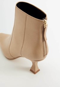 Botín beige hasta el tobillo hecho de material texturizado, con punta afilada, tacón bloque delgado y cierre con cremallera lateral. Acabado suave con detalles de costura.