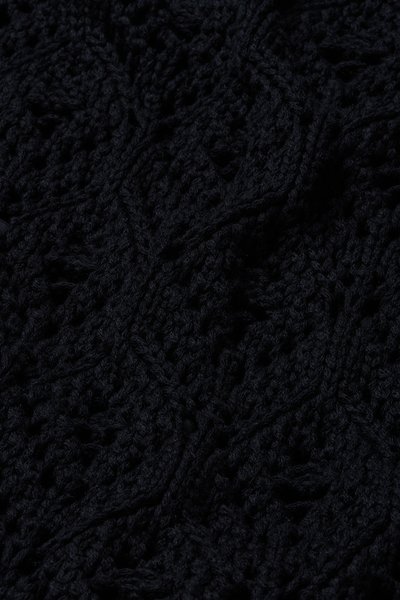 Gros plan d'un tissu noir tricoté présentant des motifs complexes en torsades et dentelle.