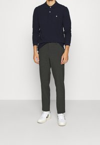 Námořnická polo košile s dlouhým rukávem a třemi knoflíky, kombinovaná se šedými přizpůsobenými kalhotami a bílými teniskami s černými akcenty.