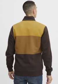 Fleecejacke mit hohem Kragen, Farbkombination in Braun, Senf und Beige, mit weicher Textur und gerippten Bündchen.