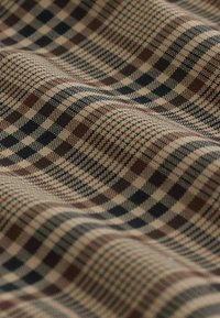 Vævet stof med et ternet mønster i beige, mørkebrun og marineblå, med en struktureret overflade og let drapering.
