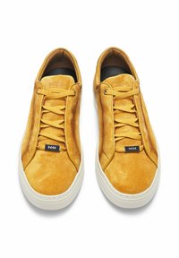 Sneaker gialle in suede con una superficie liscia, caratterizzate da un design con lacci, logo in rilievo e suola in gomma bianca.
