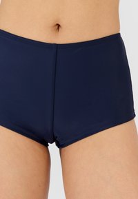 Bañador de color azul marino, confeccionado con una tela lisa y elástica. Presenta una cintura ajustada y costuras limpias, ofreciendo un ajuste cómodo.