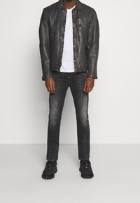 Černá kožená bunda na zip s náprsní kapsou, nošená přes bílou tričko, v kombinaci s tmavými džíny a černými teniskami.