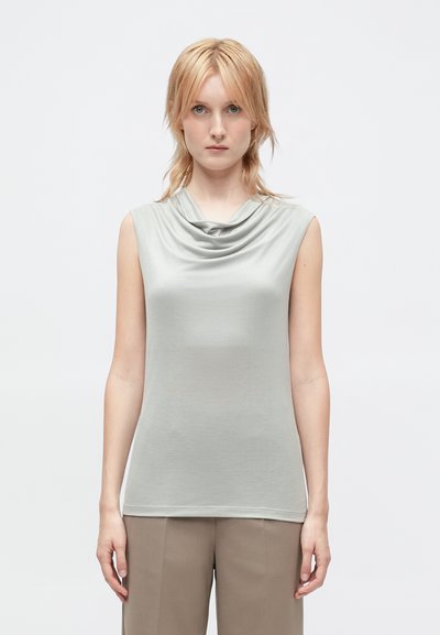 Top senza maniche grigio chiaro con scollatura drappeggiata, texture liscia e forma aderente, abbinato a pantaloni beige a vita alta.