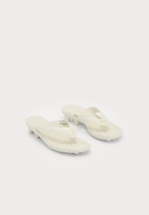 Sandali in pelle color crema di Puma con tacco basso e suole imbottite, caratterizzati da loghi dorati di Puma sulle cinghie.