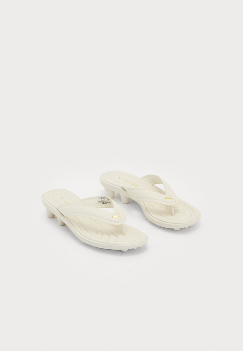 Κρεμ χρώματος σανδάλια thong της Puma με χαμηλές τακούνες και μαξιλαρωτές σόλες, διακοσμημένα με χρυσά λογότυπα Puma στις λωρίδες.