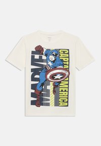 Λευκό κοντομάνικο T-shirt με το γραφικό του Captain America σε μπλε, κόκκινο και λευκό, που τον δείχνει να κρατά την ασπίδα του σε ενέργεια, με έντονο κείμενο.