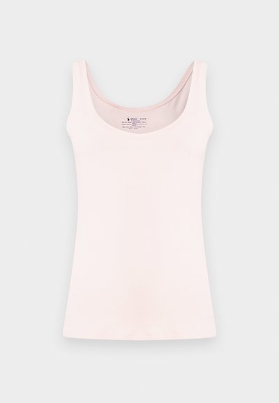 Világos rózsaszín ujjatlan trikó mély kivágással, egyszerű világosszürke háttéren bemutatva.