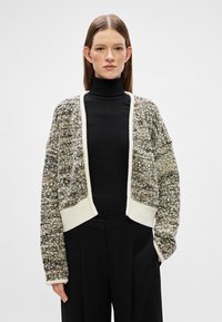 Pletený kardigan s texturovaným, vícebarevným vzorem v zemitých tónech, který má kontrastní krémový lem a otevřený přední design.