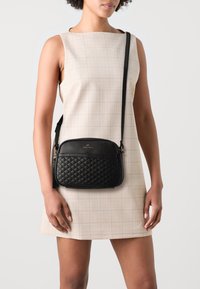 Borsa a tracolla nera in pelle con texture trapuntata, chiusura con zip e logo dorato sul davanti. Cinghia regolabile. Finitura liscia.