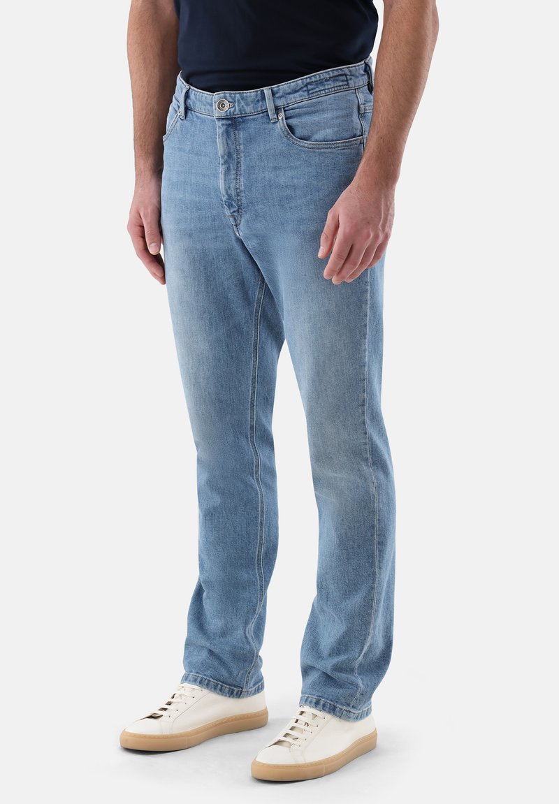 Jeans in denim azzurro chiaro con un design a taglio diritto, caratterizzati da una chiusura frontale con bottoni, tasche laterali e sottili dettagli di cucitura. Abbinati a sneakers bianche.