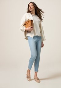 Chaqueta beige de gran tamaño con jeans azul claro. El modelo lleva un bolso color arena. Los zapatos son beige claro, de punta con correas decorativas.