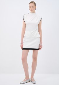 Top bianco con bordi neri, design peplum aderente, abbinato a una mini gonna bianca con orlo nero, completato con ballerine argento.