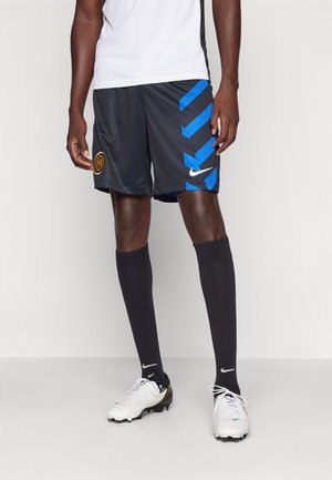 Black athletic shorts featuring blue zigzag accents and a logo, paired with black knee-length socks and white soccer cleats.