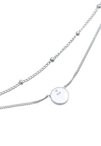 Silver necklace with two strands, featuring a circular pendant marked "925." The chains have various link styles, adding texture and detail.