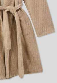 Accappatoio beige lavorato a maglia con tessuto strutturato, dotato di cintura annodata, maniche lunghe e due tasche laterali.