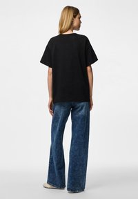 Zwarte oversized T-shirt met een ronde halslijn, gecombineerd met lichtblauwe denim jeans met brede pijpen, voorzien van een gestructureerde afwerking en lichte stiksels.