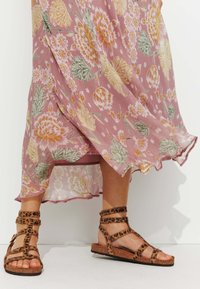 Sandales à brides en cuir imprimé léopard marron avec une semelle en liège plate, associées à une robe légère et fluide à motifs floraux roses avec un ourlet à volants.