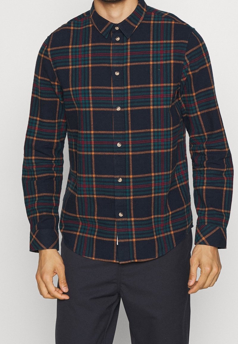 Camisa de cuadros abotonada en marino, con rayas verdes, naranjas y amarillas. Confeccionada en una tela texturizada con cuello y detalles de botones.