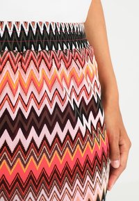 Mehrfarbiger Rock mit Zickzackmuster und schwarzem elastischem Bund. Die Farben umfassen Pink, Rot, Orange und Braun und der Stoff ist strukturiert.