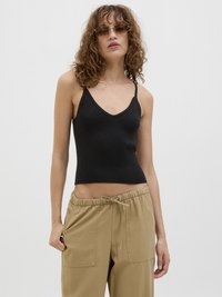 Svart ribbet tank topp med V-hals og tynne stropper, sammen med beige bukser med elastisk midje og to lommer foran.