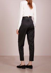 Czarne satynowe spodnie z zwężającymi się nogawkami, wysokim stanem i gładką fakturą, w połączeniu z białą bluzką z długim rękawem i czarnymi butami.