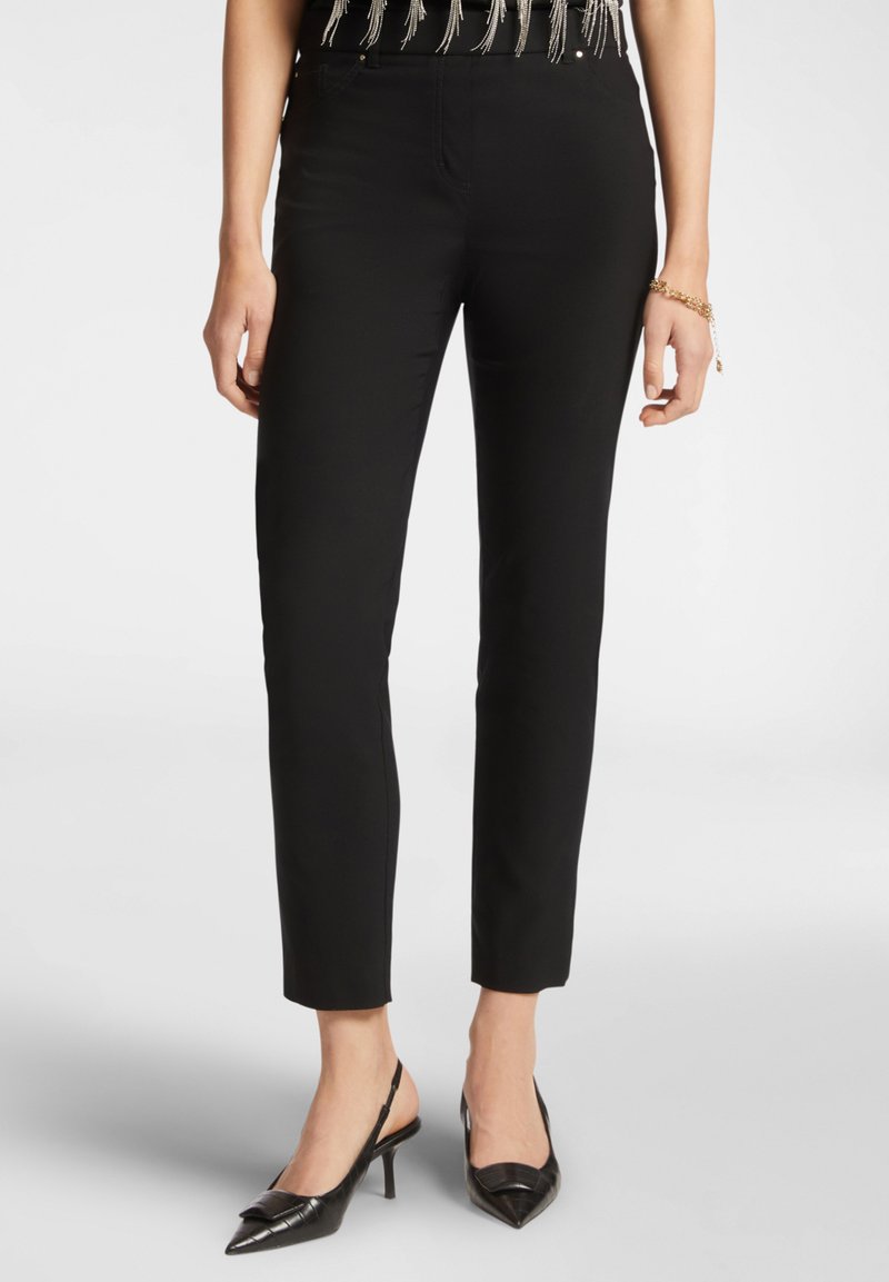 Pantaloni neri attillati con una texture liscia e taglio alla caviglia. Abbinati a tacchi slingback a punta con motivo coccodrillo.