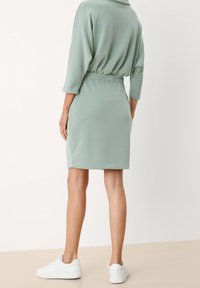 Mintunvihreä lyhyt mekko, jossa on kireä vyötärö, kolmivartiset hihat ja pehmeä tekstuuri, yhdistettynä valkoisiin tennareihin.