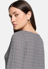 Zwart-wit gestreepte top met een ronde halslijn en lange mouwen, gemaakt van een soepele stof met een geometrisch ontwerp.