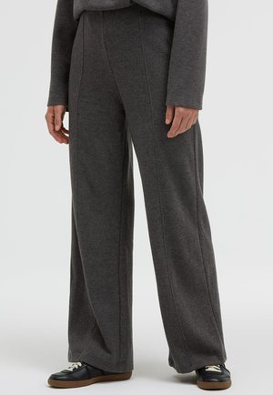 Graue Sweatpants mit weitem Bein aus weichem Stoff, mit vertikalen Nähten und einem bequemen Bund, kombiniert mit schwarzen Sneakern.