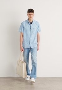 Camisa de mezclilla de manga corta azul claro, jeans azules claros a juego, zapatillas blancas y un bolso de mano crema. Diseño simple, ajuste casual.