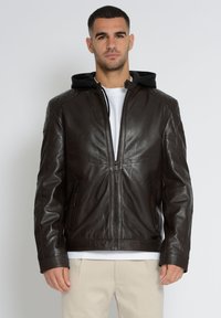 Brun læderjakke med quiltede skuldre, frontlynlås og aftagelig sort hætte. Har sidelommer med lynlås og en glat finish.