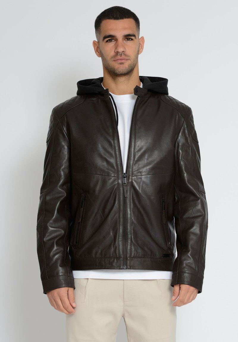 Brun læderjakke med quiltede skuldre, frontlynlås og aftagelig sort hætte. Har sidelommer med lynlås og en glat finish.