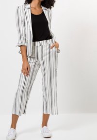 Completo a righe con base bianca e strisce verticali nere, tessuto leggero, pantaloni a cropped e giacca aderente. Include sneakers bianche.