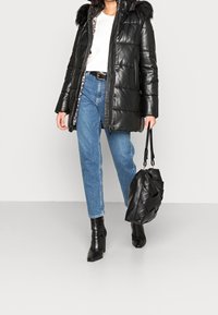 Černá prošívaná parka s kapucí lemovanou kožešinou, nošena přes bílé tričko a modré džíny. Dalš�í černá prošívaná kabelka a kotníkové boty s krokodýlím vzorem.