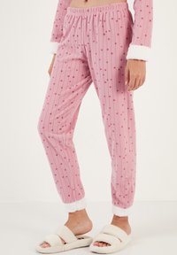 Pantalones de pijama rosas con rayas verticales y pequeños patrones de estrellas. Cuentan con una cintura elástica y suaves puños blancos. Hechos de material de felpa.