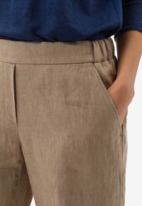 Pantalon en lin beige à coupe décontractée, taille élastique, poches latérales et finition texturée subtile.