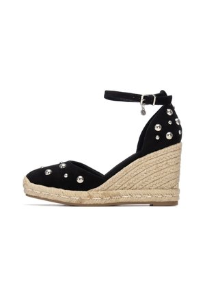 Alpargata cuña negra con correa en el tobillo, tachuelas plateadas en la parte superior y plataforma de yute trenzado.