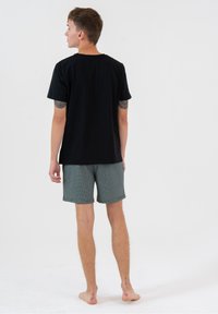 Czarny bawełniany T-shirt w połączeniu z kraciastymi zielonymi szortami. Szorty mają luźny krój oraz boczne kieszenie, charakteryzują się gładką teksturą.