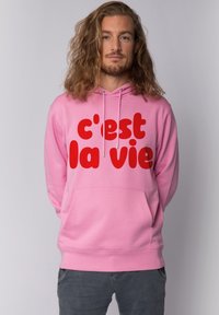 Roze hoodie met een groot rood tekstlogo dat "c'est la vie" zegt. Bevat een voorzak en verstelbare trekkoorden op de capuchon.