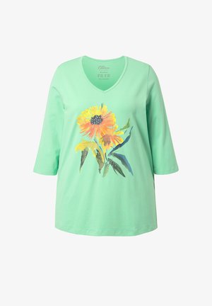Maglietta verde menta con scollo a V e maniche a tre quarti, con un grande disegno floreale in stile acquerello nei toni del giallo e arancione, con foglie verdi.