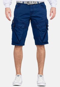 Shorts cargo bleu marine en coton, dotés de plusieurs poches, d'une taille ajustée et d'une couture contrastante. Portés avec des baskets blanches.