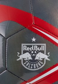 Pallone da calcio nero e rosso con superficie testurizzata, pannelli esagonali e un logo ben visibile del Red Bull Salisburgo con accenti bianchi.