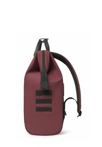 Zaino rosso e nero realizzato in un tessuto liscio e resistente. Presenta una parte superiore arrotolata, spallacci regolabili e tre fasce nere verticali sui lati.