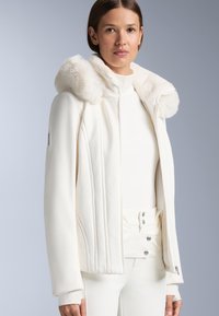 Jachetă albă cu glugă căptușită cu blană, având textură matlasată și un design ajustat, asortată cu un top alb cu guler înalt și pantaloni asortati.