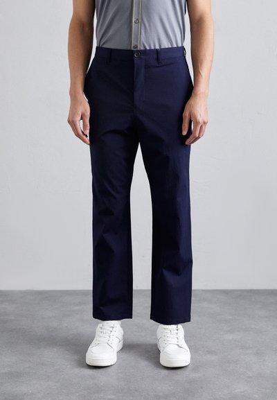 Pantaloni di colore blu navy realizzati in tessuto testurizzato, con design a gamba dritta e chiusura frontale con un solo bottone. Indossati con sneakers bianche.