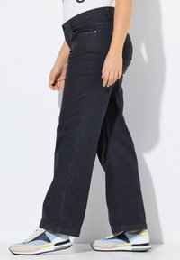 Donkerblauwe denim wijde broek met een gladde textuur, zijzakken en een hoge taille; gecombineerd met meerkleurige sportschoenen.